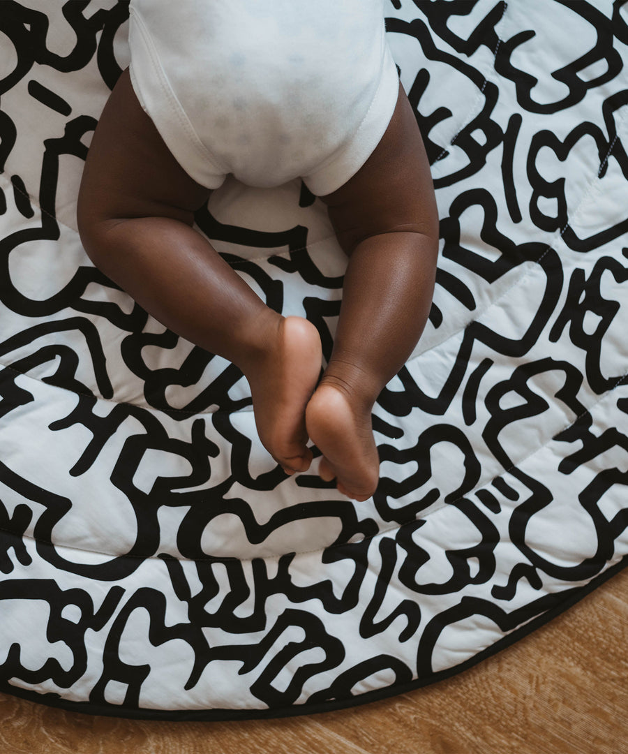 A baby lying down and looking at the 'Brazil' print on the Etta Loves X Keith Haring Reversible Organic Cotton Baby Play Mat