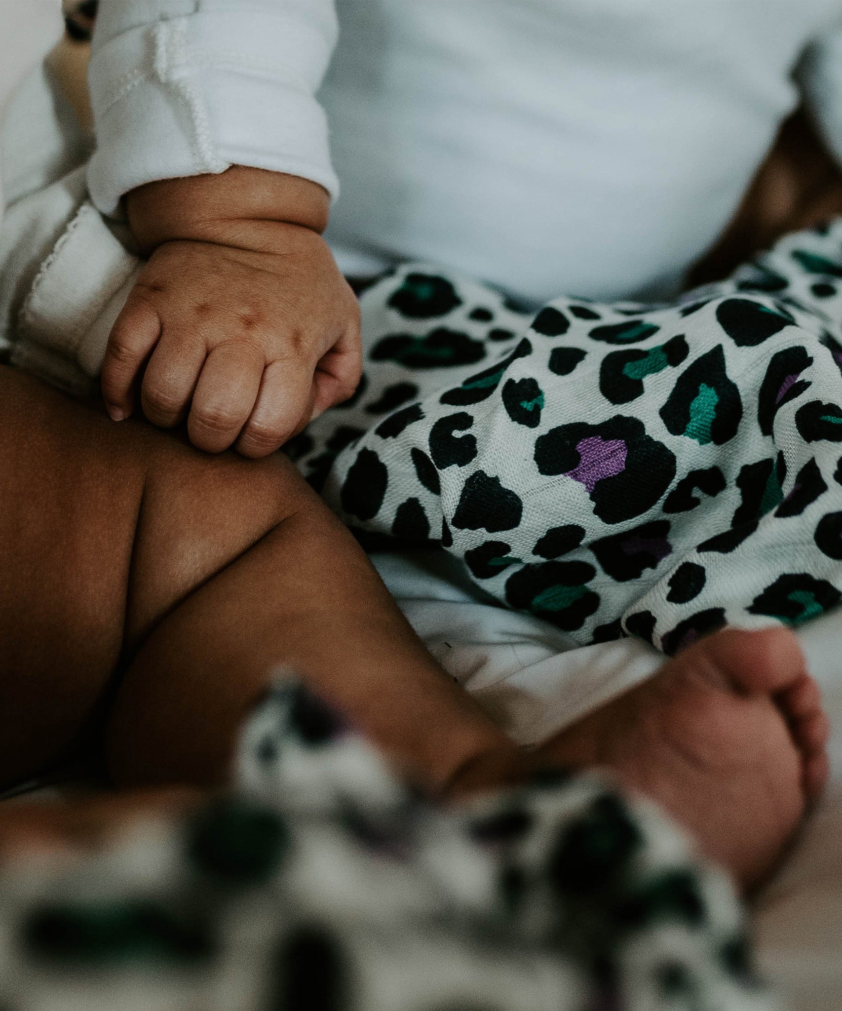 A baby looking up at the purple and green Leopard spot print on the Etta Loves Organic Cotton Baby Muslin Squares 3 Pack - Leopard