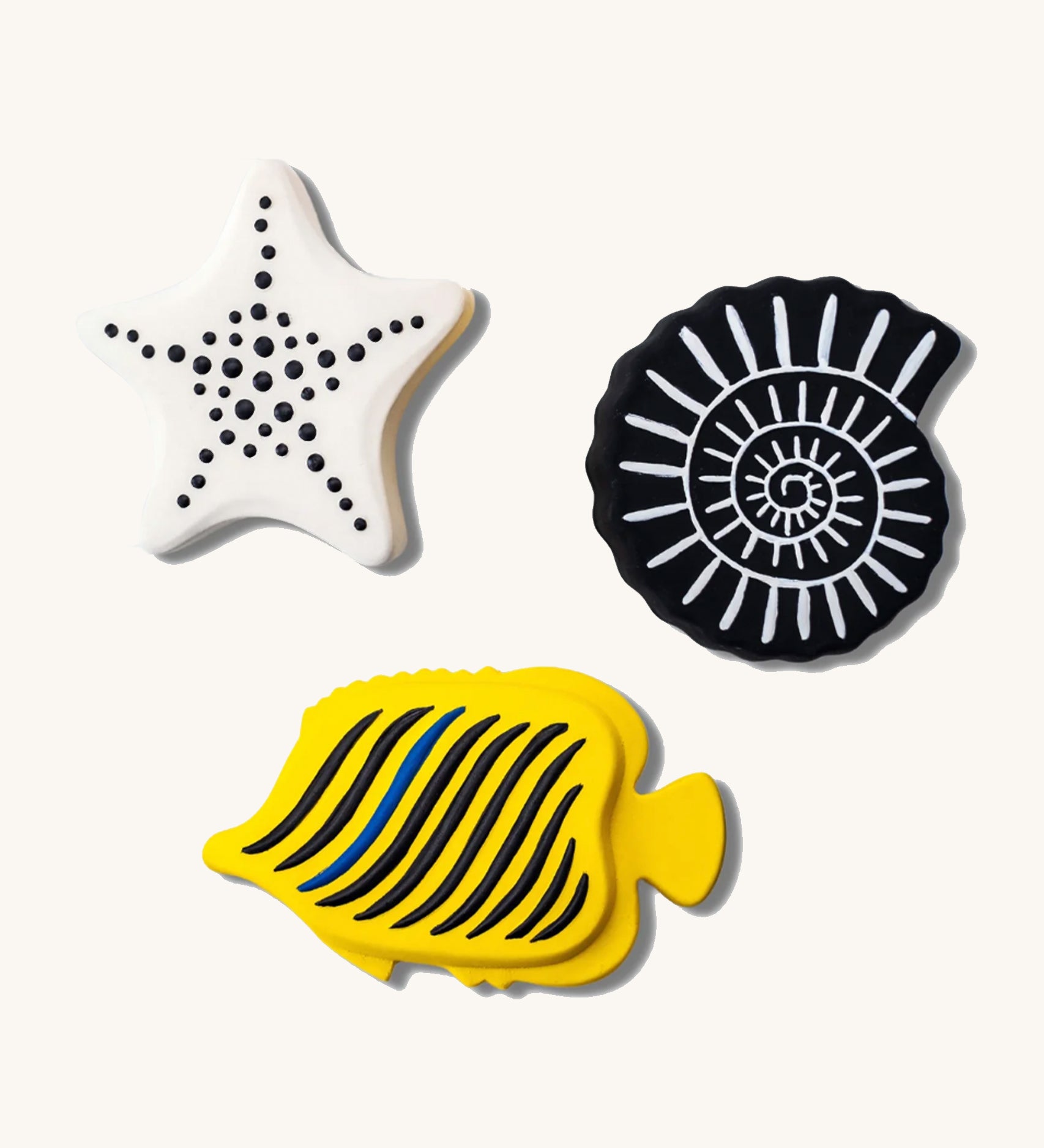 Etta Loves Natural Rubber Animal Sensory Bath Toys - 3 Pack which includes a white starfish with black spots, a black seashell with white lines, and a yellow fish with black stripes and one blue stripe, on a cream background