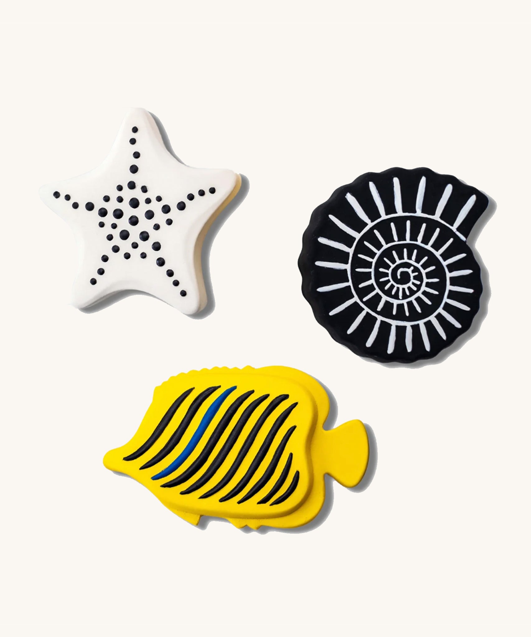 Etta Loves Natural Rubber Animal Sensory Bath Toys - 3 Pack which includes a white starfish with black spots, a black seashell with white lines, and a yellow fish with black stripes and one blue stripe, on a cream background