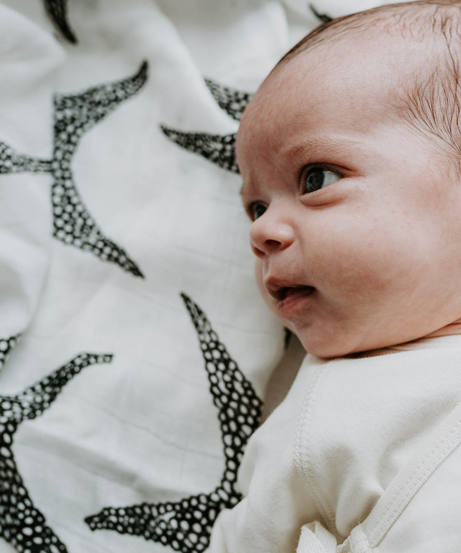 A toddler surrounded with the Etta Loves Organic Cotton Muslin Squares 3 Pack - Animal Print