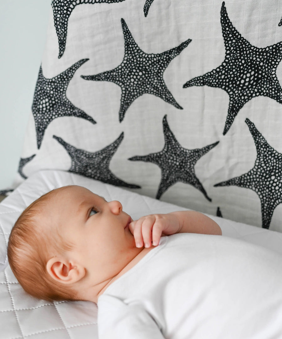 A baby lying down and looking up at the XL Starfish muslin cloth 