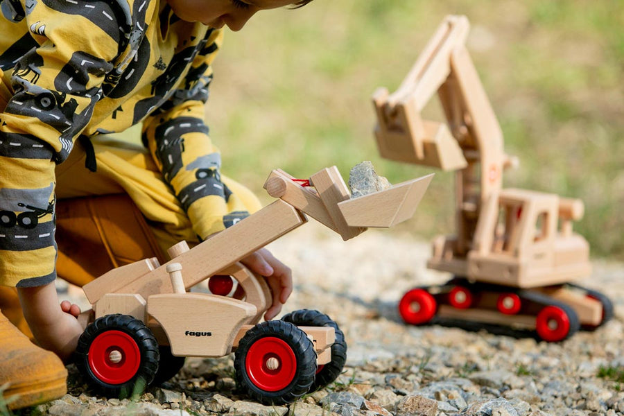 Child playing with the Fagus large wooden telescopic loader toy on some grey gravel