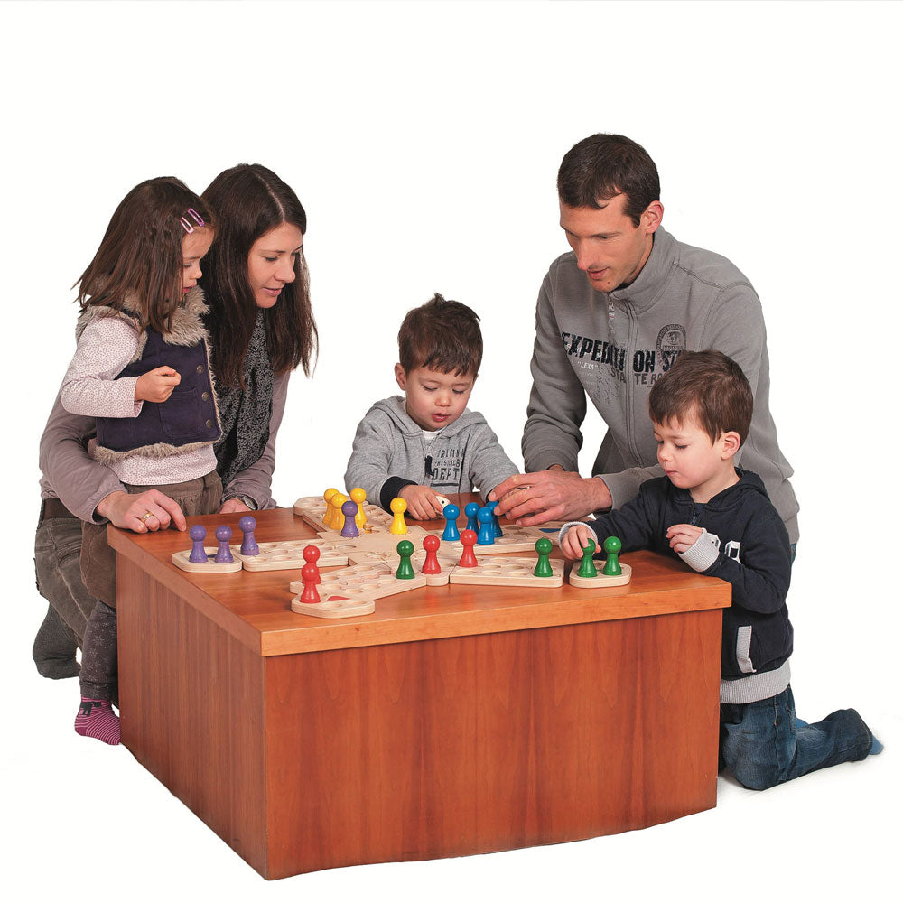 Family gathered around a small table playing the Fagus wooden enchanted playground board game on a white background