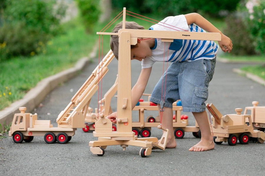 Child playing with the Fagus wooden crane toy on a concrete path