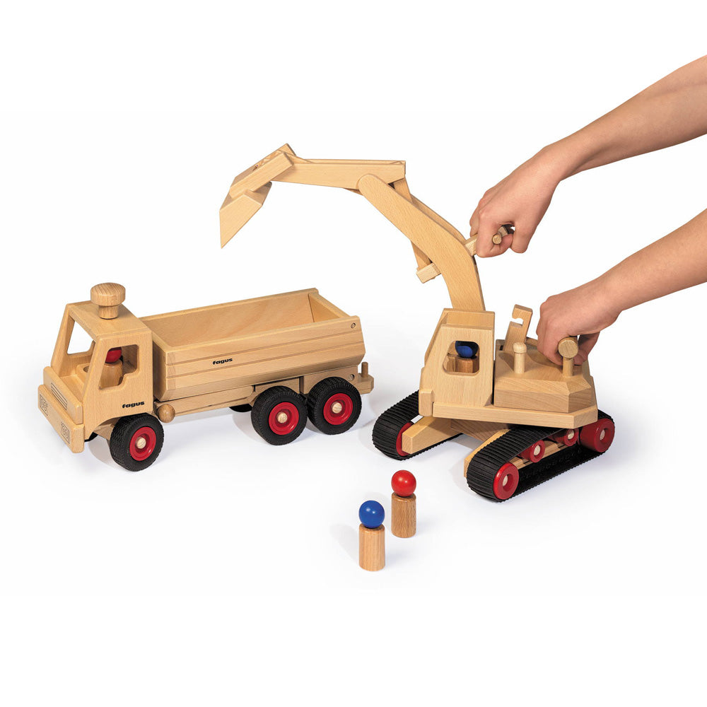 Hands moving the Fagus wooden digger toy over the Fagus wooden tipper truck on a white background