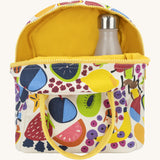 Fluf zip lunch bag in white opened showing the yellow inner lining and a bottle packed inside. Outside of the bag is a design of different coloured fruits with a yellow handle and zip detail on a cream background.