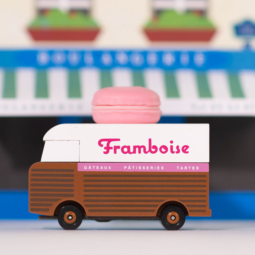 Picture of the Framboise Candylab Candyvan with a high street store in the background. It is a 1960s style brown and white van with a pink Raspberry Macaron on the roof.