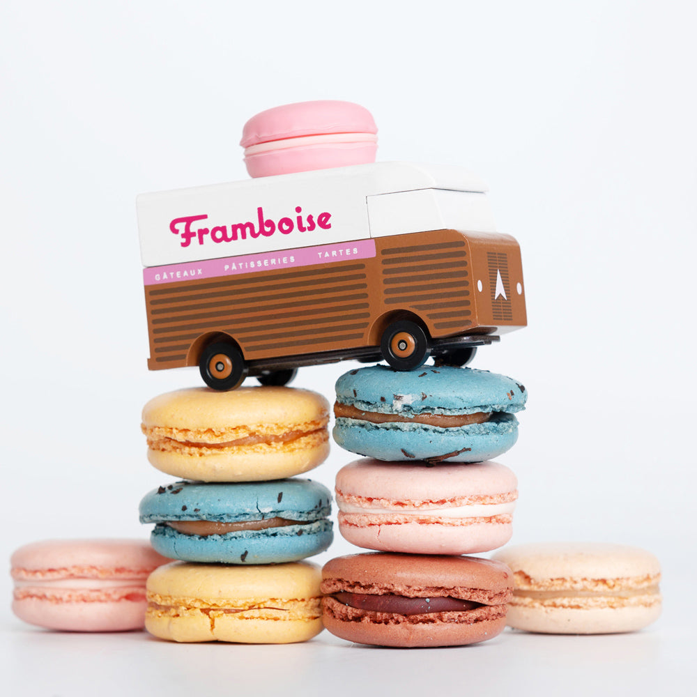 Picture of the Framboise Candylab Candyvan. on top of a pile of macarons. It is a brown and white van with a pink Raspberry Macaron on the roof.