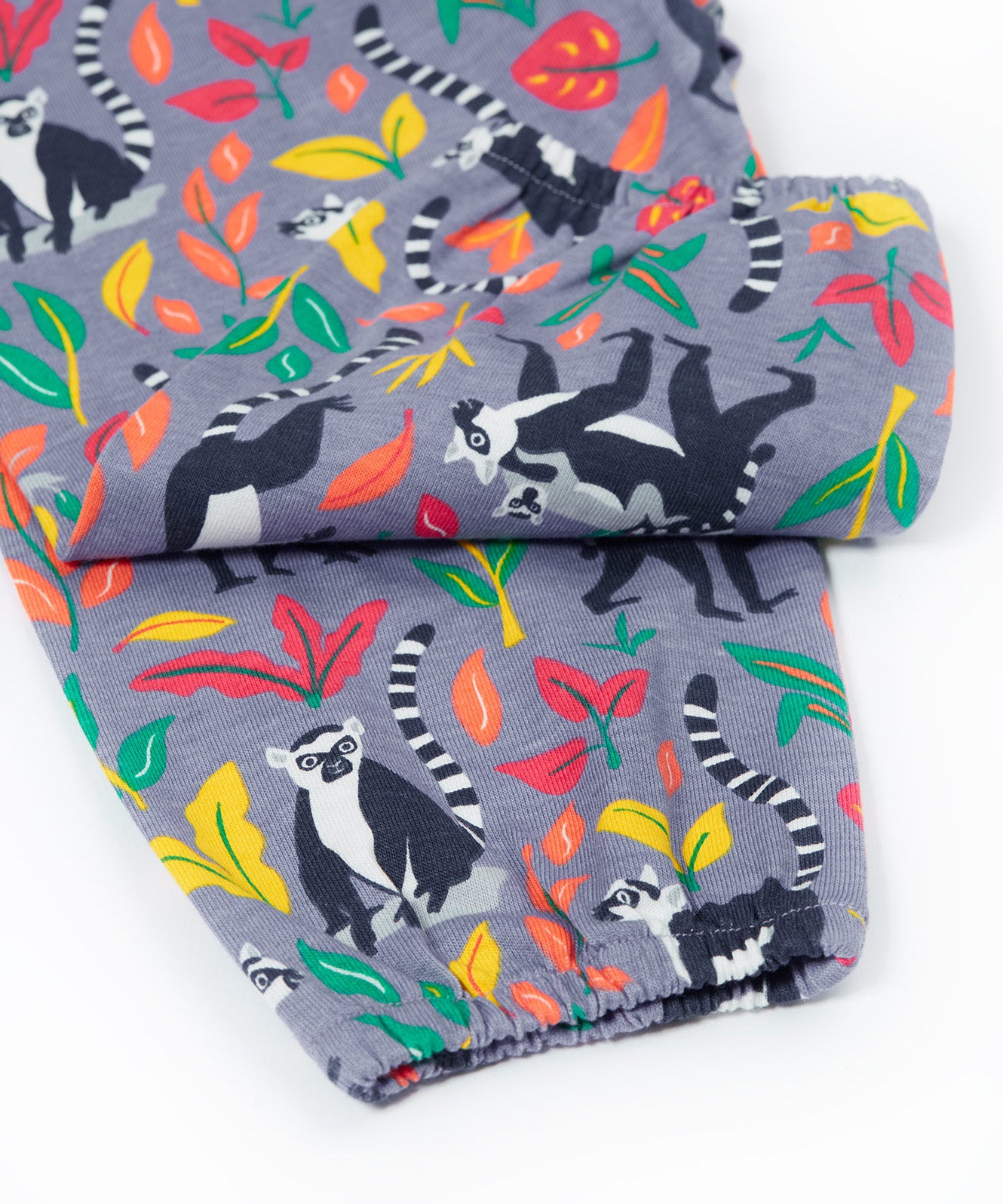 Close up of the Frugi Rowenna outfit, lemur laugh showing the printed lemurs next to different coloured leaves and leg cuff details on the bottoms  on light purple organic cotton fabric