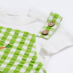 Close up of the Frugi kids Alfred dungarees outfit showing the white sleeve t-shirt and green gingham shoulder straps with the button detail on organic cotton fabric