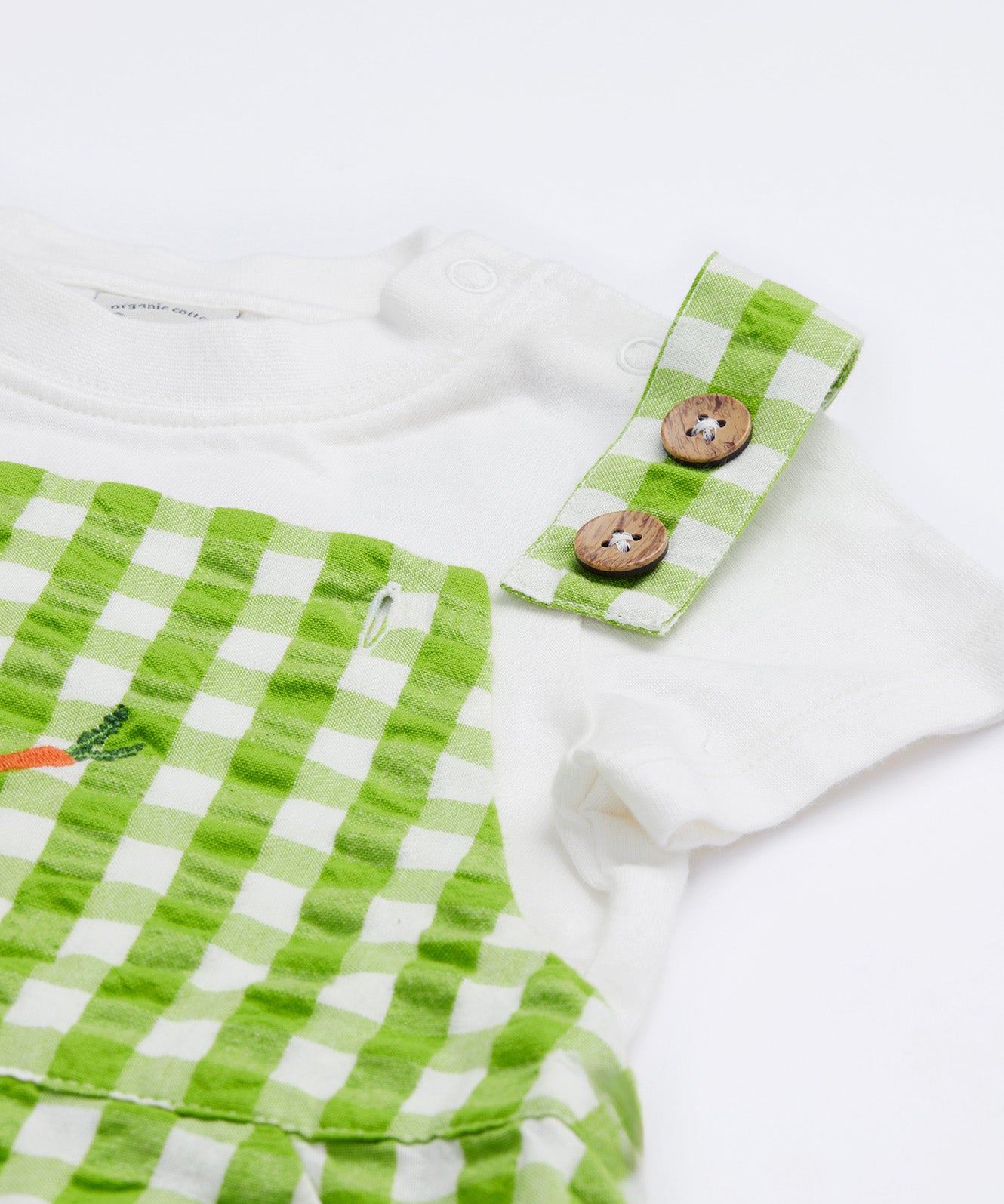 Close up of the Frugi kids Alfred dungarees outfit showing the white sleeve t-shirt and green gingham shoulder straps with the button detail on organic cotton fabric