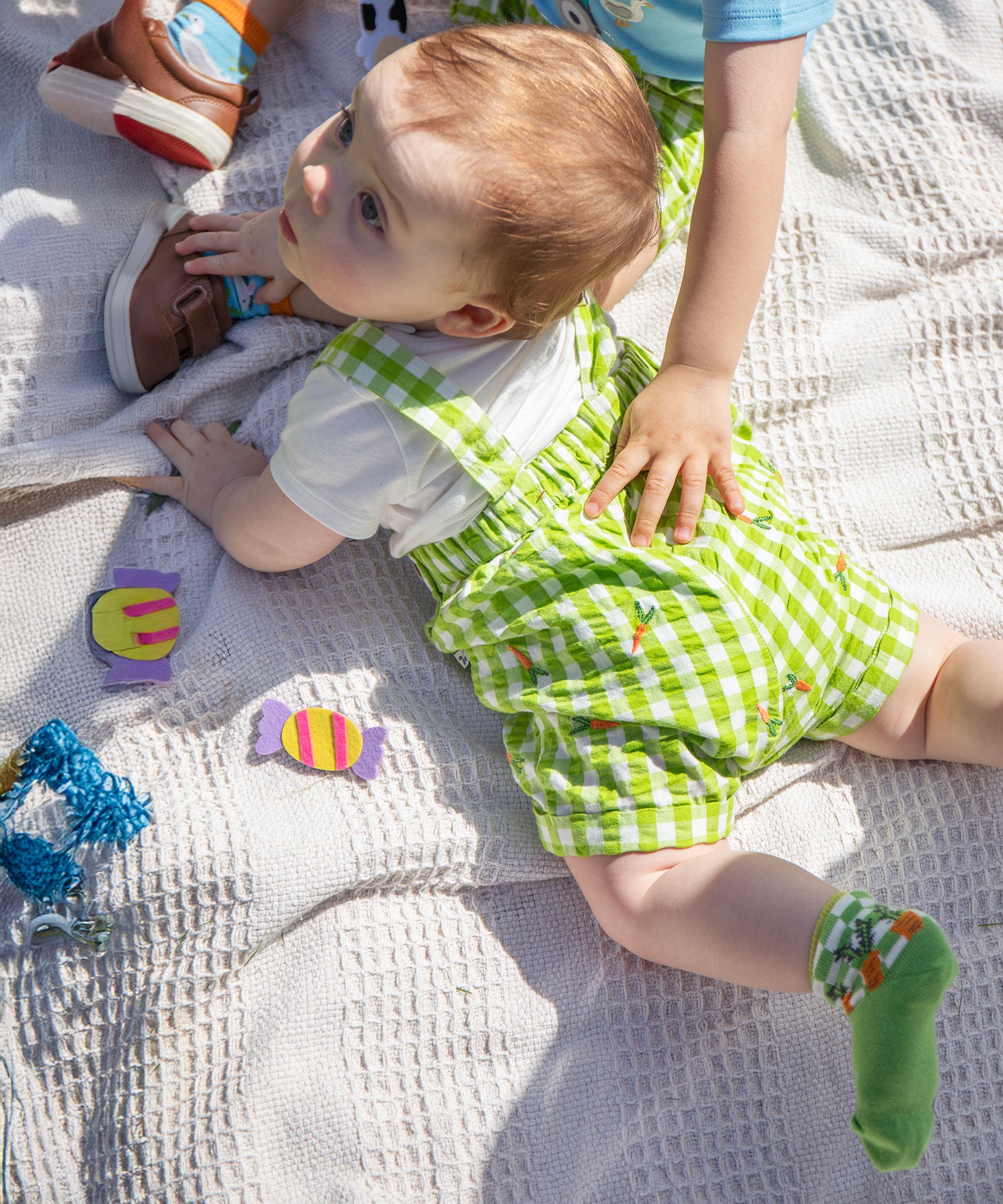 A baby laying on their front wearing the Frugi Alfred Dungaree Outfit - 
 a Macaw green coloured Gingham with Carrots design