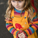 A child wearing the the Frugi Babipur yellow cord dungarees, the photo shows a close up of the red elephant applique on the front. 