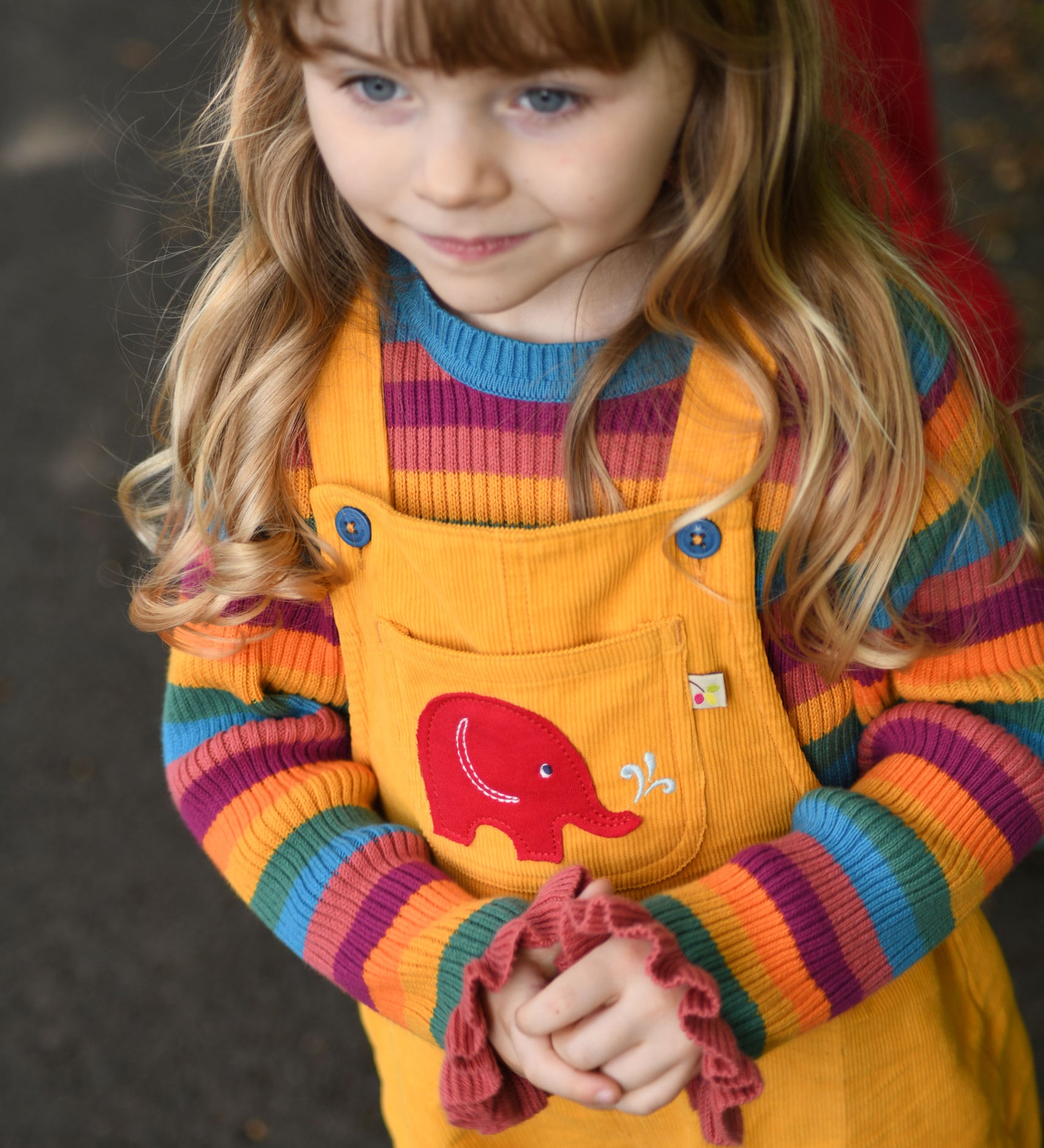 A child wearing the the Frugi Babipur yellow cord dungarees, the photo shows a close up of the red elephant applique on the front. 