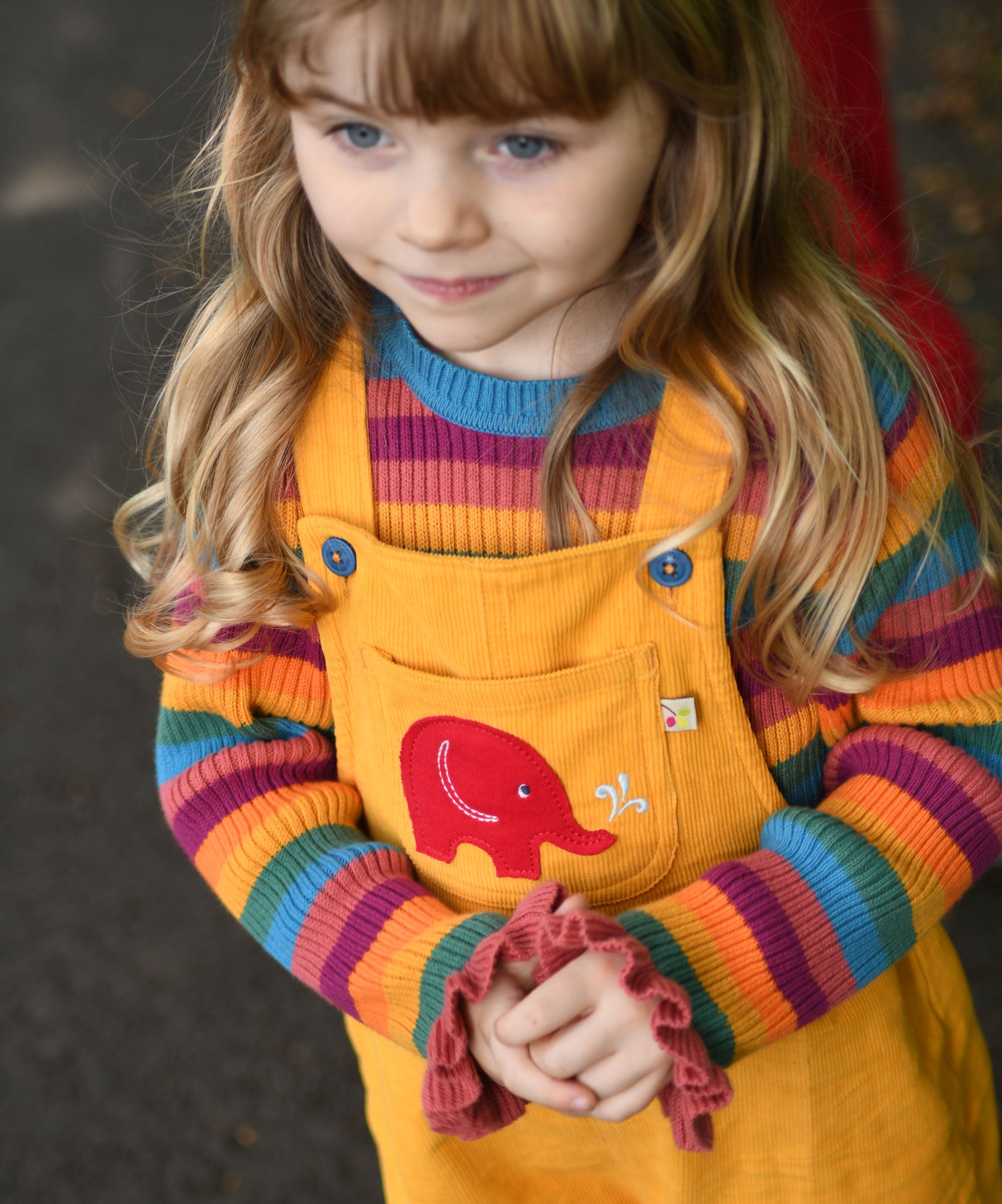 A child wearing the the Frugi Babipur yellow cord dungarees, the photo shows a close up of the red elephant applique on the front. 