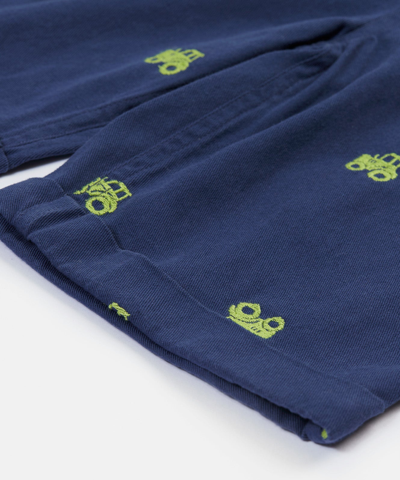 Close up of the Frugi baby short navy tractor dungarees. Showing the turn up detail and green tractor embroidery on navy organic cotton fabric.