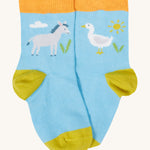 Close up of the baby farm field sock. Showing the grey donkey and white goose print and a light orange elasticated cuff  mustard heel and toe contrast panel on light blue organic cotton fabric. 