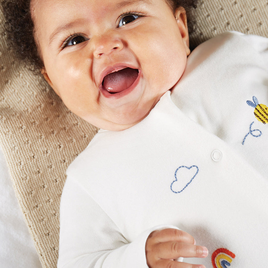 A baby lies on a mat wearing the Frugi Embroidered Babygrow - Buzzy Bee.