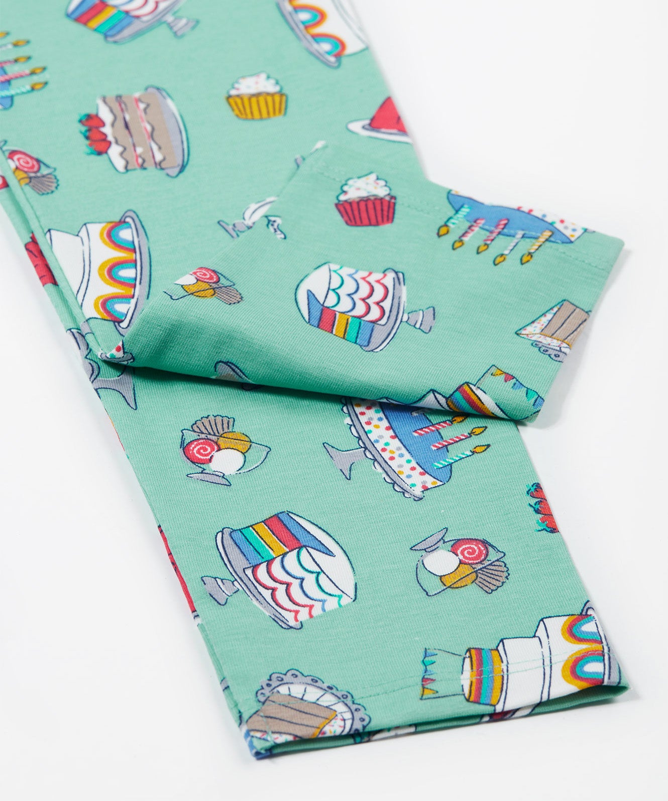 A close up of the Frugi kids let's bake libby leggings. Showing the different cakes, puddings and ice creams design leg cuffs on a light green organic cotton fabric