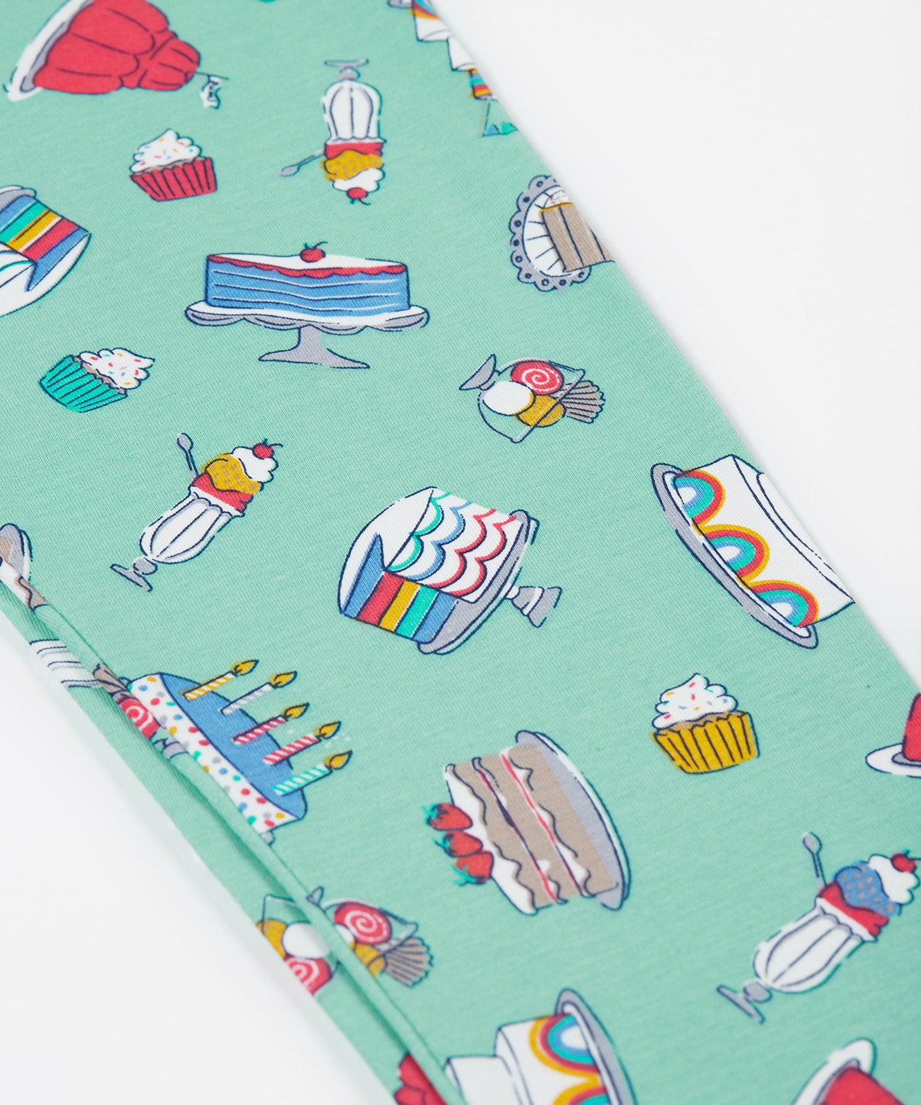 A close up of the Frugi kids let's bake libby leggings. Showing the different cakes, puddings and ice creams designs on a light green organic cotton fabric