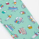 A close up of the Frugi kids let's bake libby leggings. Showing the different cakes, puddings and ice creams designs on a light green organic cotton fabric