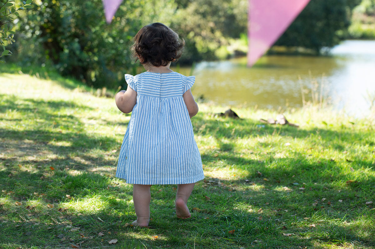 Child wearing the Frugi  Beach Hut Blue Stripe Birdie Body Dress showing the back of the dress