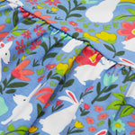 Close up of the Frugi kids Bella dress bunny bounce. Showing a collection of white rabbits printed with different coloured flowers and bright rainbows on light blue organic cotton fabric