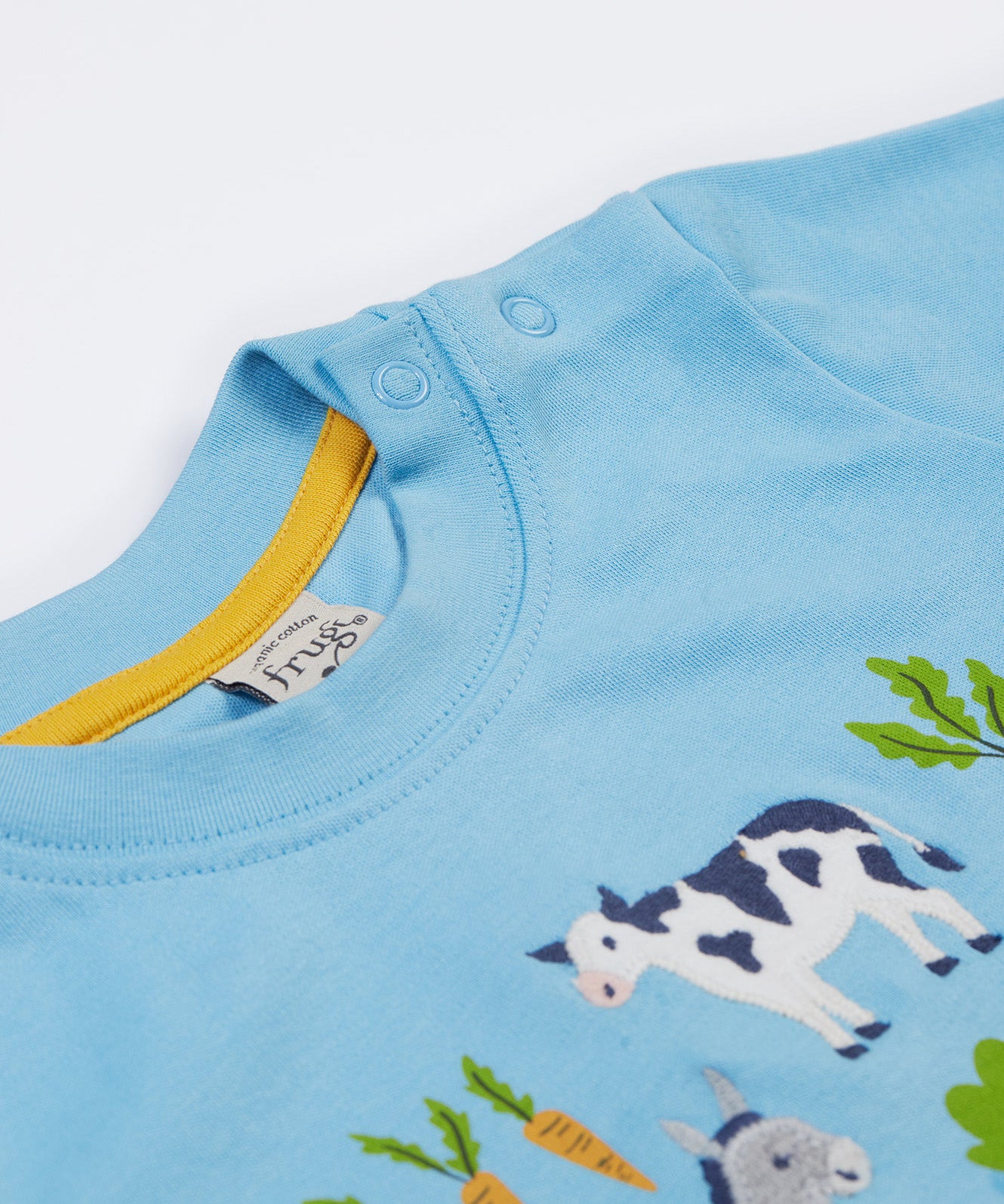 A close up of the Frugi kids bluebird farm life t-shirt  showing the shoulder popper fasteners for easy fitting and light blue neck trim with a yellow trim on the inside on light blue organic cotton fabric.