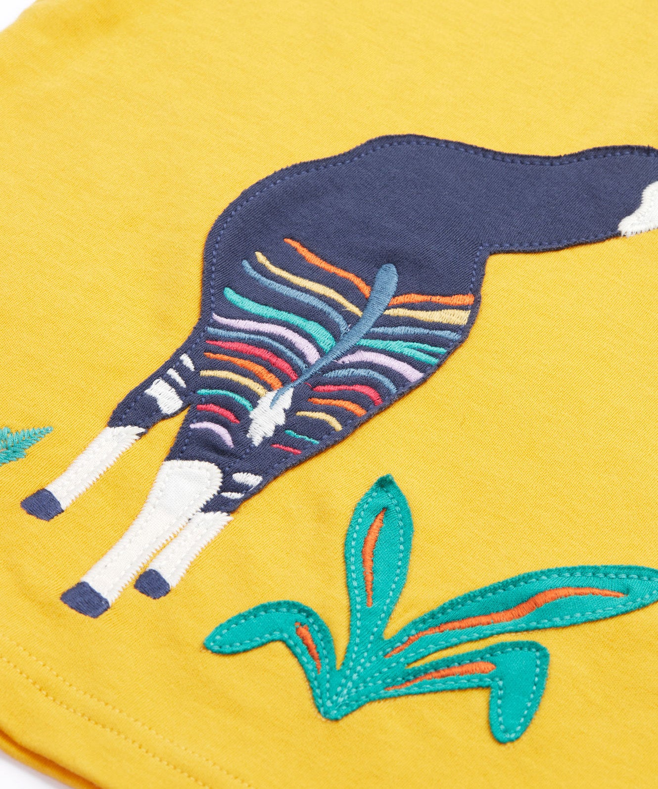 Close up of the Frugi kids bumblebee okapi short sleeve t-shirt. showing the body of the okapi animal appliqué next to green plants on yellow organic cotton fabric