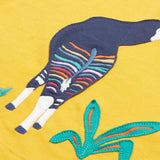 Close up of the Frugi kids bumblebee okapi short sleeve t-shirt. showing the body of the okapi animal appliqué next to green plants on yellow organic cotton fabric