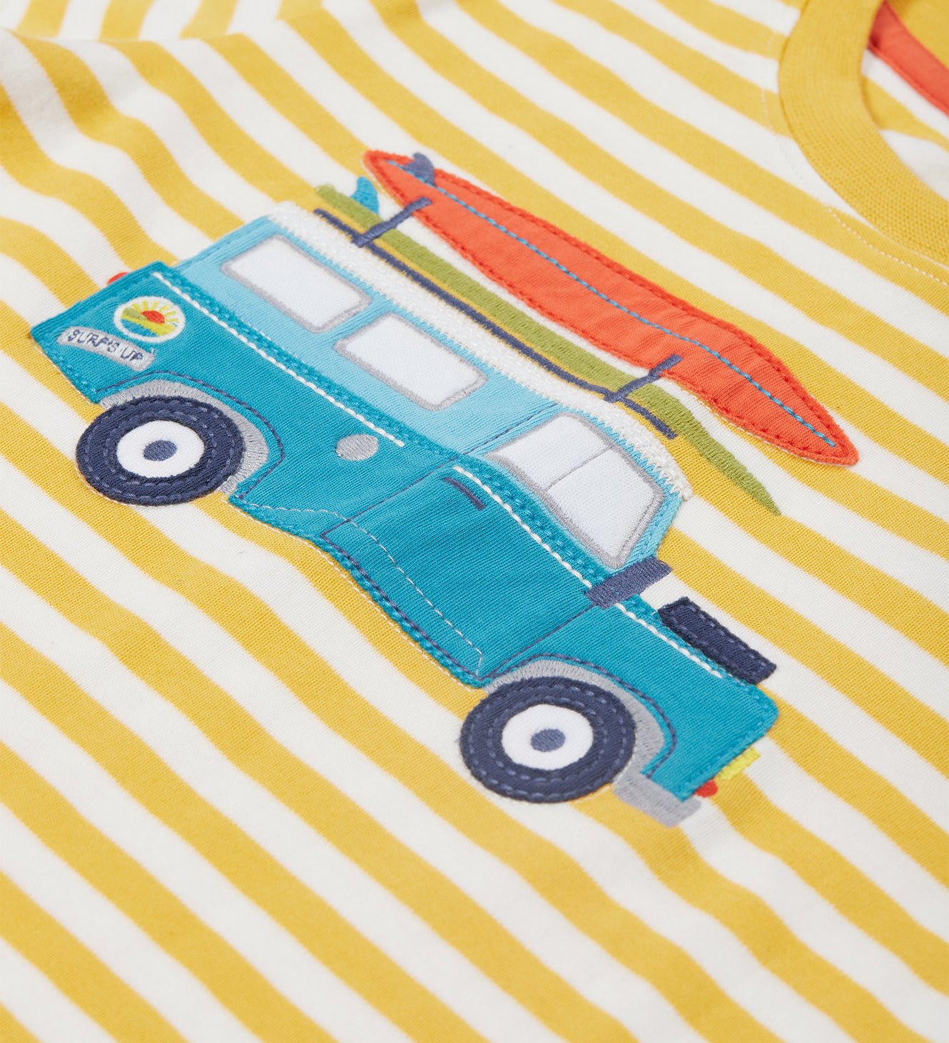 Close up of the Frugi campervan short sleeve t-shirt. Showing a blue camper van appliqué tractor with a orange surfboard on top on a yellow and white striped organic cotton fabric 