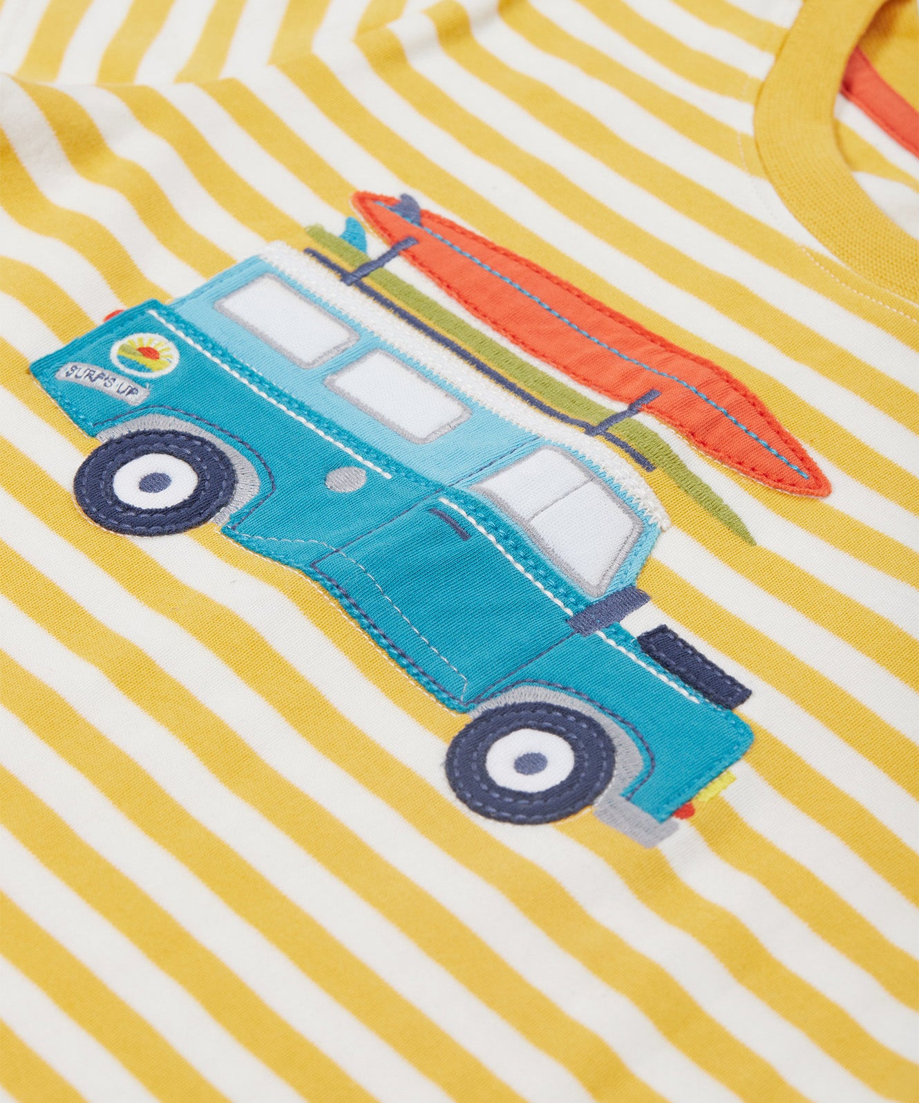 Close up of the Frugi campervan short sleeve t-shirt. Showing a blue camper van appliqué tractor with a orange surfboard on top on a yellow and white striped organic cotton fabric 