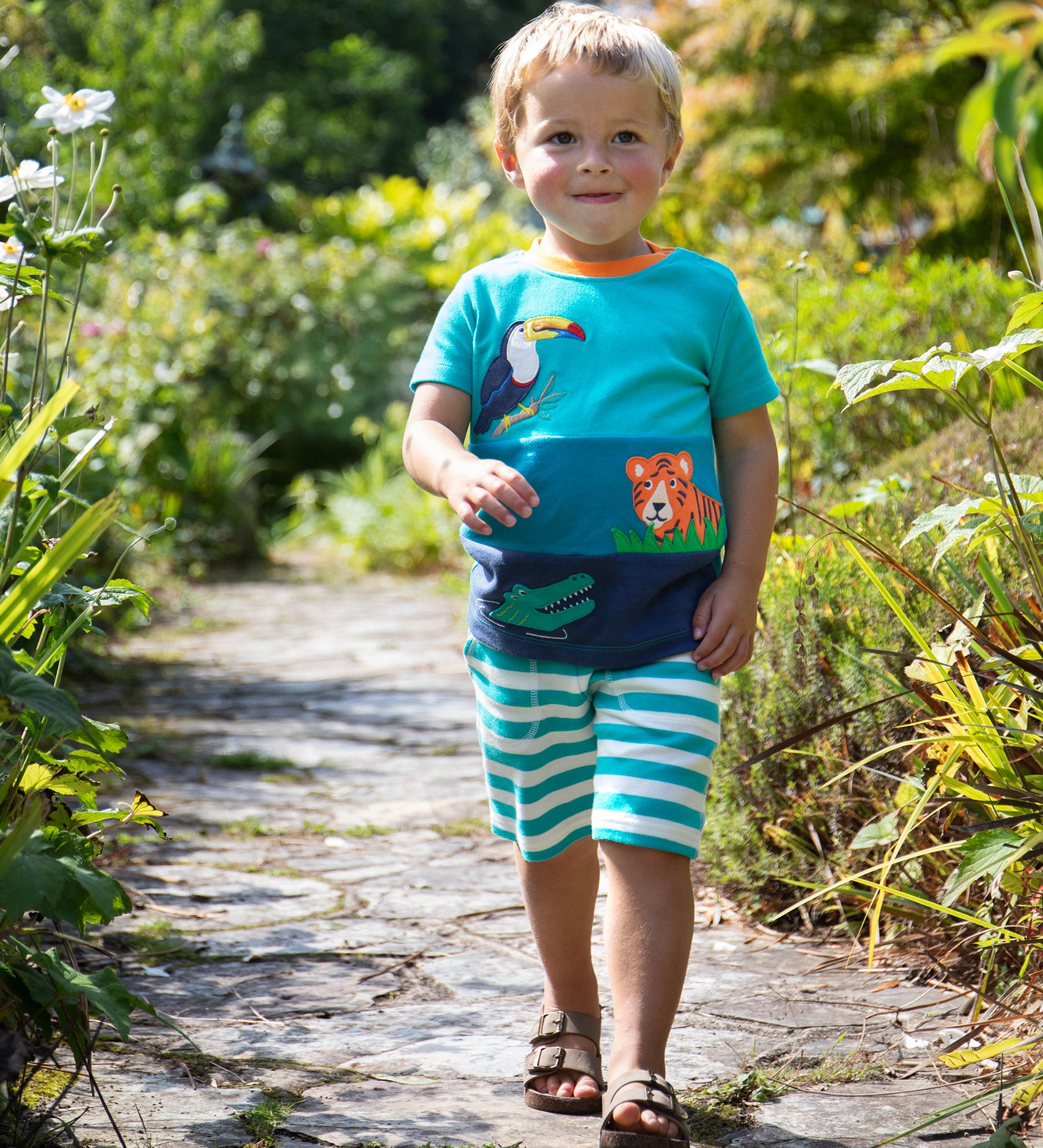 A child wearing the Frugi Canopy Land Sea Penryn Panel T-shirt with Frugi sea moss stripe Sunny Shorts.