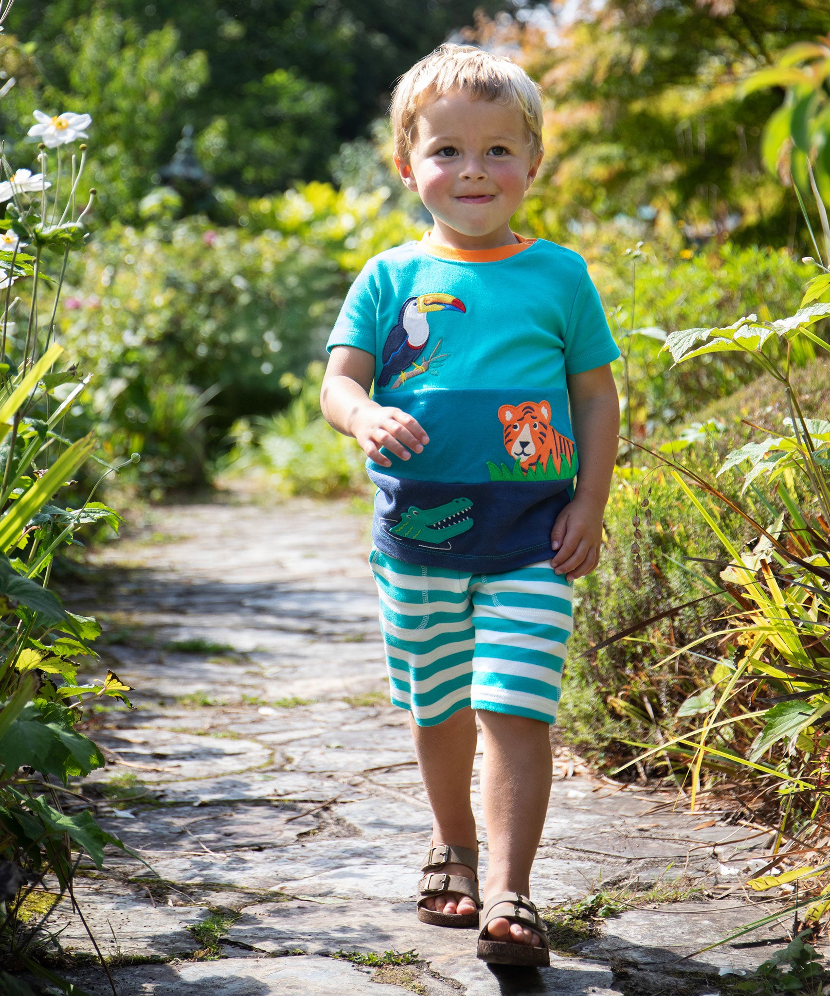 A child wearing the Frugi Canopy Land Sea Penryn Panel T-shirt with Frugi sea moss stripe Sunny Shorts.