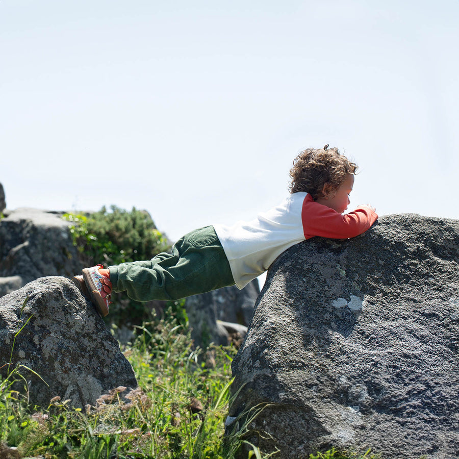 A child plays outdoors wearing the Frugi Luke Raglan Top - Stay Wild / Paprika.