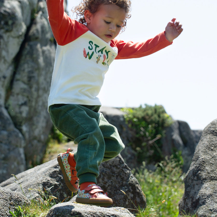 A child plays outdoors wearing the Frugi Luke Raglan Top - Stay Wild / Paprika.