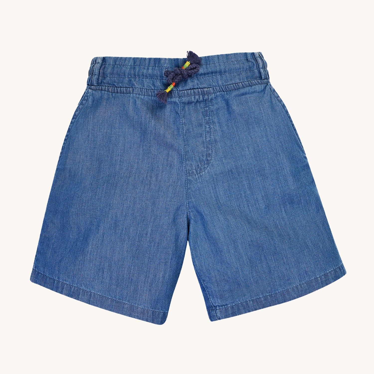 Frugi Organic Cubert Chambray Denim Shorts. A soft and durable organic cotton navy denim shorts, with four pockets, an adjustable navy drawcord and elasticated waistband, on a cream background