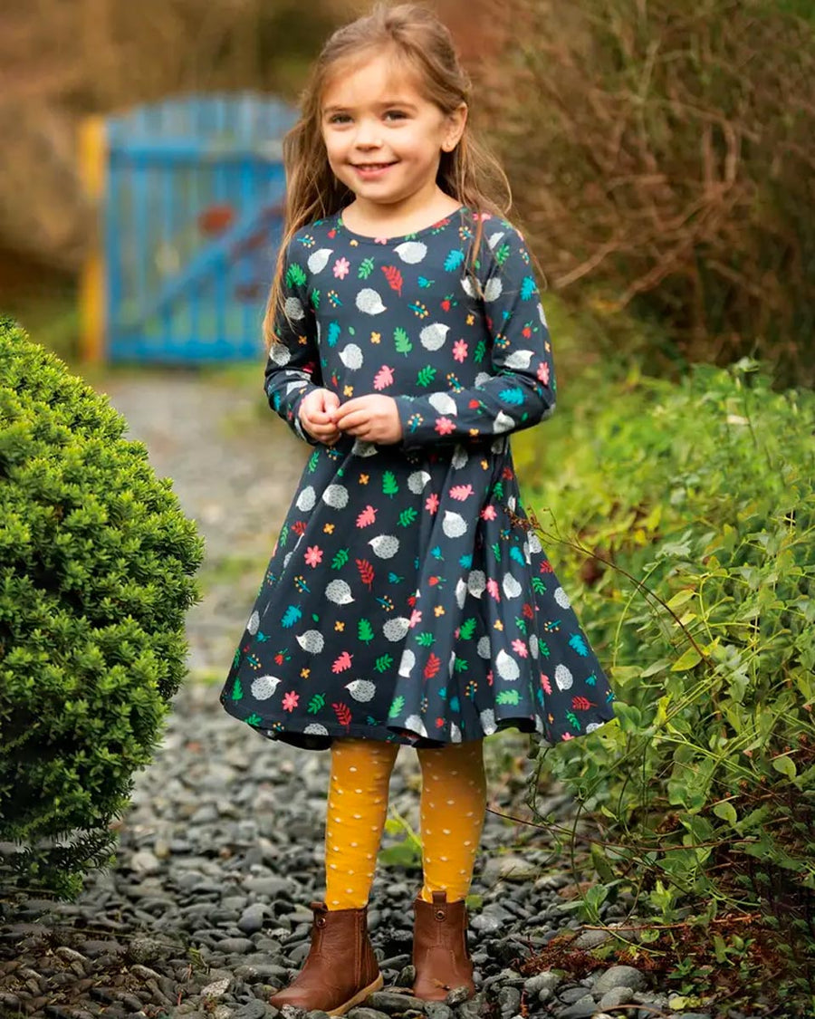 Young girl stood on a stone path wearing a Frugi dress and the bumble bee spotty norah tights