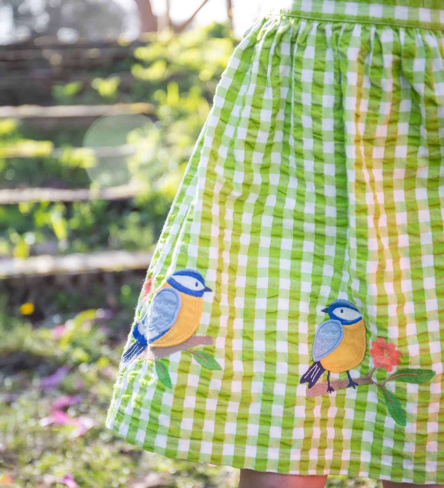 A close up of the embroidered bird applique detail on the bottom of the Frugi Children's Organic Cotton Macaw Gingham  Birds Zaria Dress 