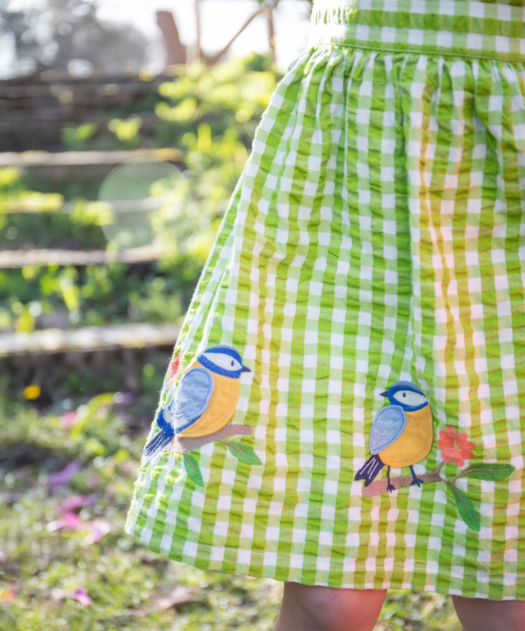 A close up of the embroidered bird applique detail on the bottom of the Frugi Children's Organic Cotton Macaw Gingham  Birds Zaria Dress 