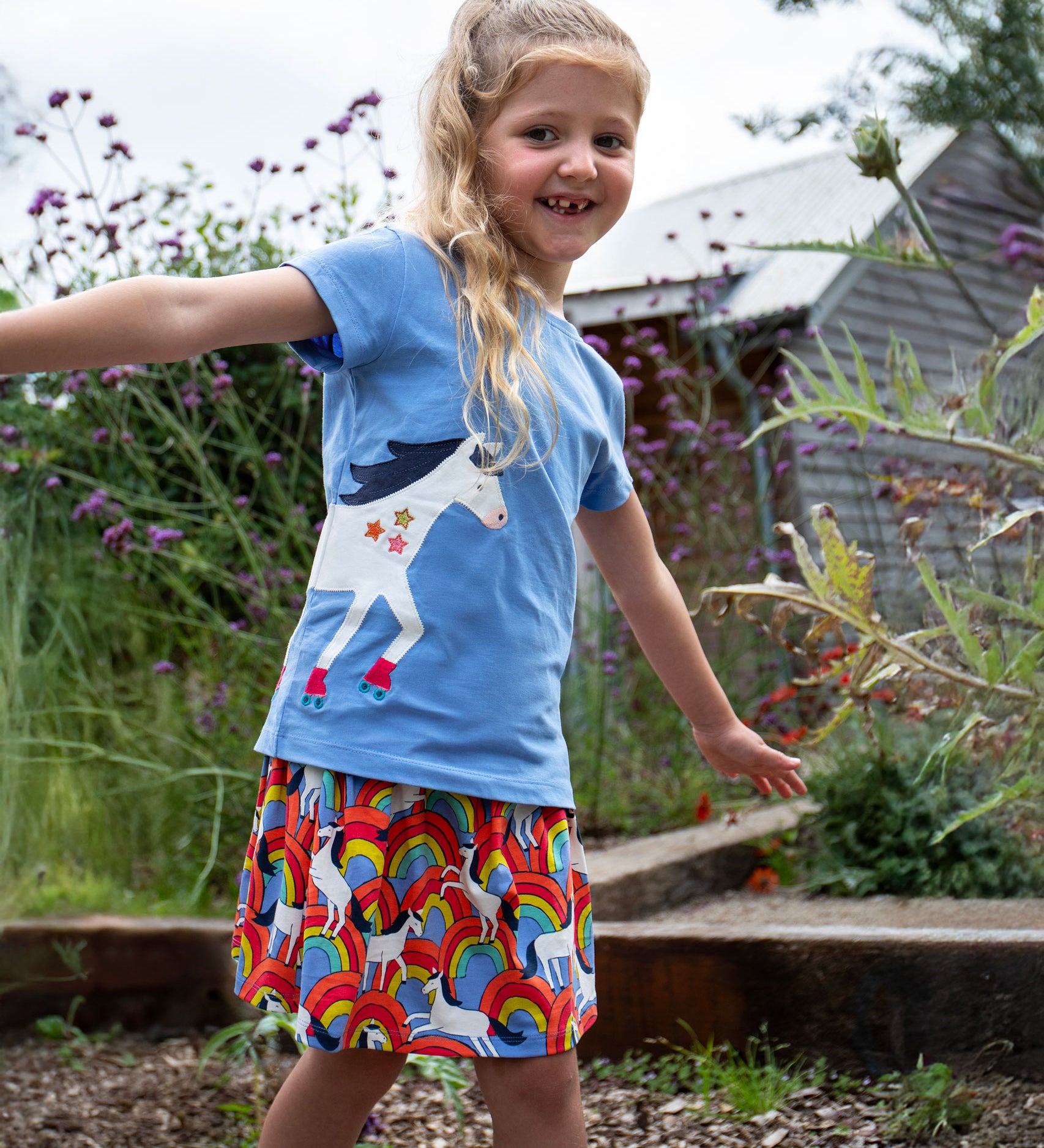 A child wearing the All Over The Rainbow print organic cotton skort with a cornflower blue horse applique t-shirt..