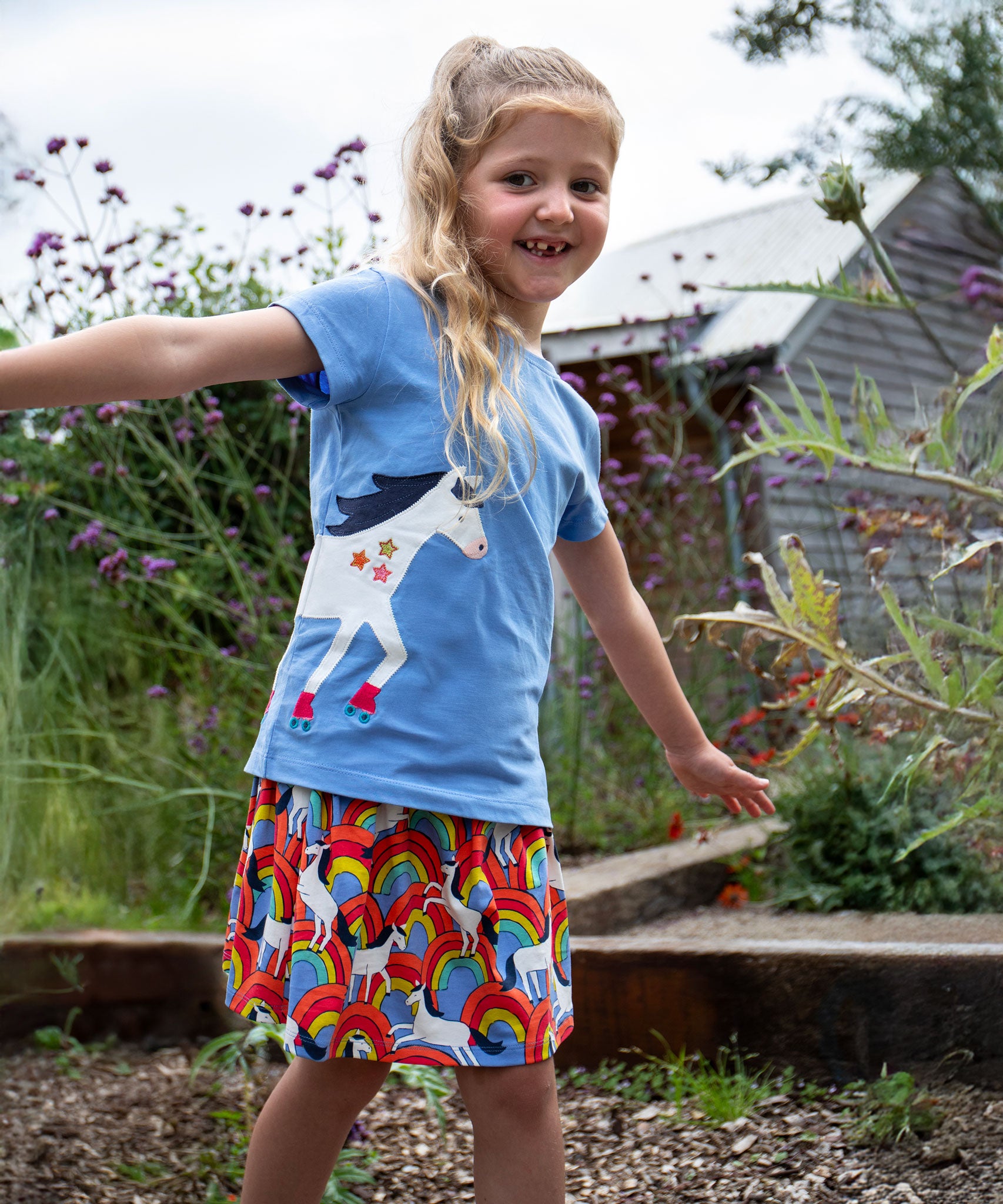 A child wearing the All Over The Rainbow print organic cotton skort with a cornflower blue horse applique t-shirt..