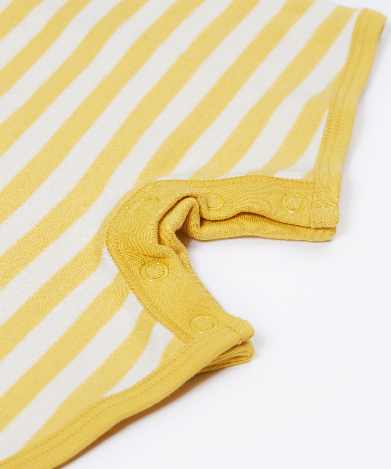 Close up of the Frugi kids crocodile rue romper. Showing the poppers on the inside of the legs for easy fitting on yellow and white striped organic cotton fabric