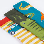 A close up of the Frugi kids crocodile rock my socks 3 pack - GOTS organic cotton socks which features a teal sock with crocodiles, a green crocodile sock and a yellow and white stripe sock with a campervan.