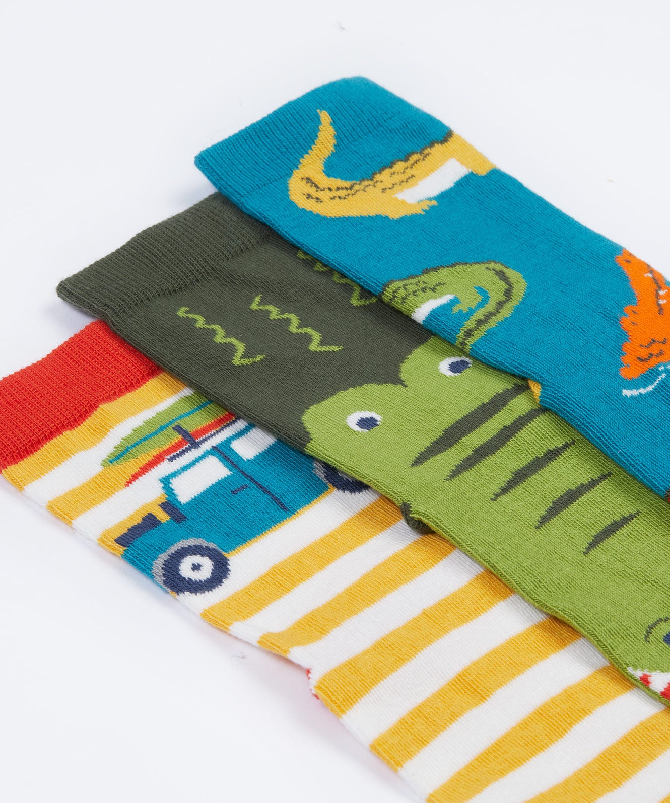 A close up of the Frugi kids crocodile rock my socks 3 pack - GOTS organic cotton socks which features a teal sock with crocodiles, a green crocodile sock and a yellow and white stripe sock with a campervan.