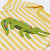 Close up of the Frugi kids crocodile rue romper. Showing the appliqué detail of a green crocodile on yellow and white striped organic cotton fabric