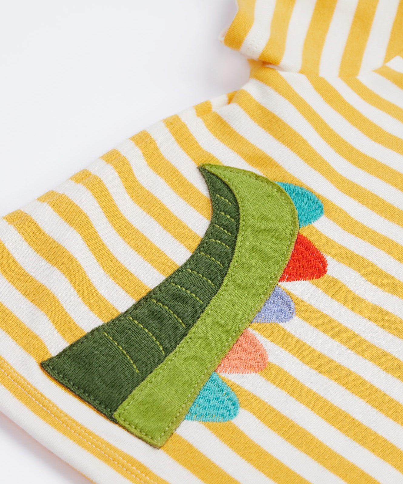 A close up of the Frugi kids wrap around crocodile outfit. Showing the back of the t shirt with the tail of the crocodile applique on yellow and white stripe organic cotton fabric