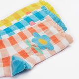 A close up of the Frugi kids Freya frilled gingahm socks - Showing the blue gingham with pink daisy sock, a yellow gingham with light orange daisy sock and a light orange gingham and blue daisy sock on organic cotton fabric