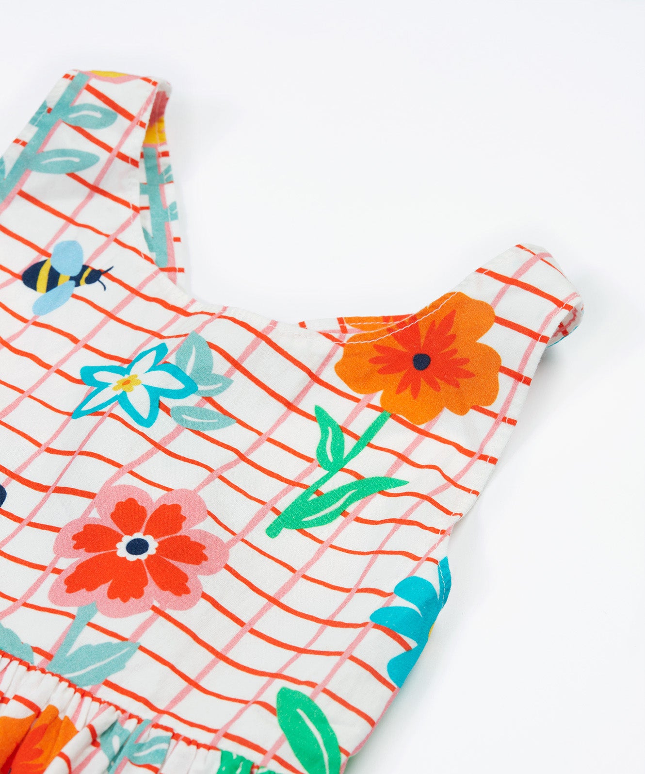 Close up of the Frugi kids Delpi paint a floral dress. Showing the shoulder strap detail, coloured flowers and yellow bees on white check with red outline organic cotton fabric